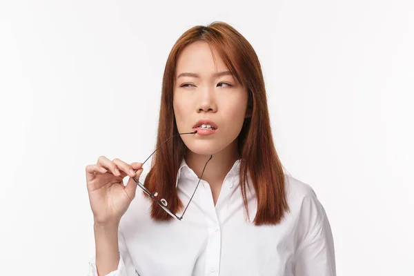 Bureau, concept d'affaires et de style de vie. Gros plan portrait d'une jeune femme d'affaires soupçonneuse et réfléchie qui enlève des lunettes, mord son rebord et plisse en réfléchissant, fond blanc — Photo