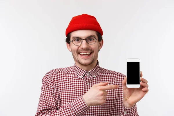 技術と人々の概念。クローズアップ肖像画幸せな笑顔若いひげを生やしたヒップスター男携帯電話を保持し、スマートフォンのディスプレイを指して、アプリをダウンロードすることをお勧めします、素晴らしい試合で自慢 — ストック写真