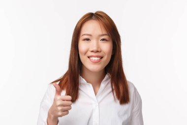 Yakın plan gülümseyen mutlu Asyalı kadın beyaz gömlekli, aferin, aferin, baş parmak hareketi yap ya da kabul et, başını salla, beyaz arka planda dur