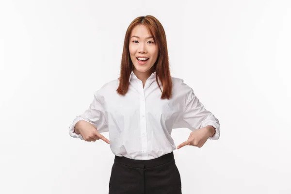 Ritratto di bella donna asiatica sorridente in camicia bianca e gonna nera invitare check-out prodotto, puntando il dito verso il basso e guardando la fotocamera, dare consigli, promuovere mostrando progetto — Foto Stock