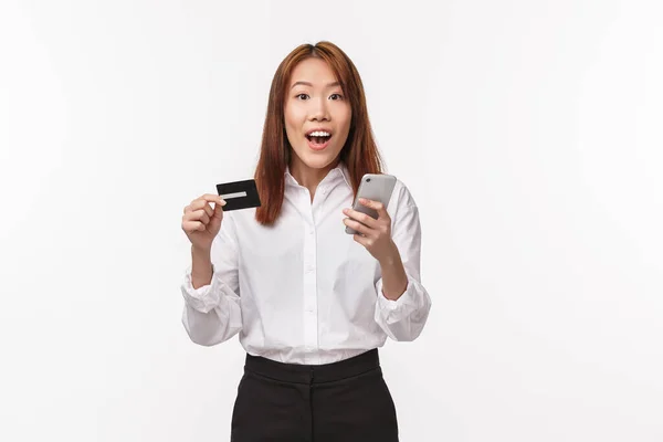 Retrato de mujer asiática linda excitada en camisa y falda, sosteniendo teléfono móvil y tarjeta de crédito, haciendo pedido por Internet, compras en línea, uso de depósito bancario, cuenta de registro en la tienda, fondo blanco — Foto de Stock