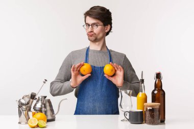 Barmen, kafe çalışanı ve barmen konsepti. Komik, aptal bir erkek çalışanın portresi göğsünde portakal tutarken meme gibi somurtuyor, beyaz arka planda duruyor, kahve yapıyor.