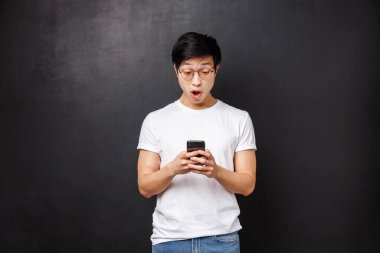 Teknoloji, aletler ve insan konsepti. Şaşırmış ve etkilenmiş Asyalı yakışıklı adam internetten okuduğu heyecan verici haberlere tepki veriyor, elinde cep telefonu, akıllı telefon ekranı ile eğleniyor.