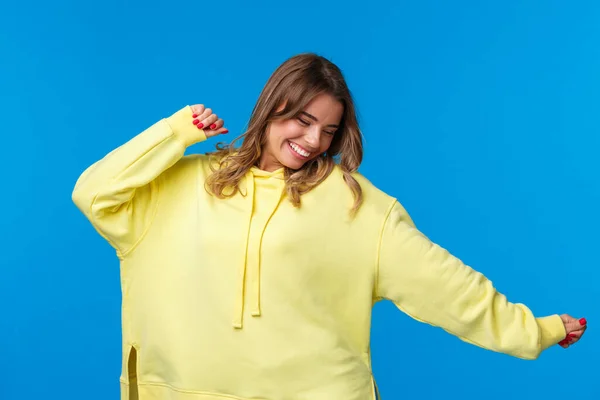 Avslappnad och bekymmerslös glad blond flicka att ha kul, dansa till musik, njuta av fritid med vänner på awesome fest eller konsert, flytta händerna i sidled blunda och le, blå bakgrund — Stockfoto