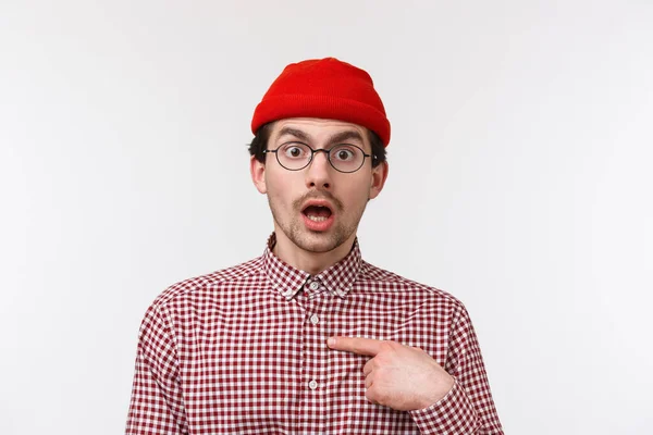 Close-up retrato surpreendido jovem hipster cara em óculos e gorro olhando com descrença, apontando-se indeciso, não sei se a pessoa de verdade mencionou-o, de pé fundo branco — Fotografia de Stock