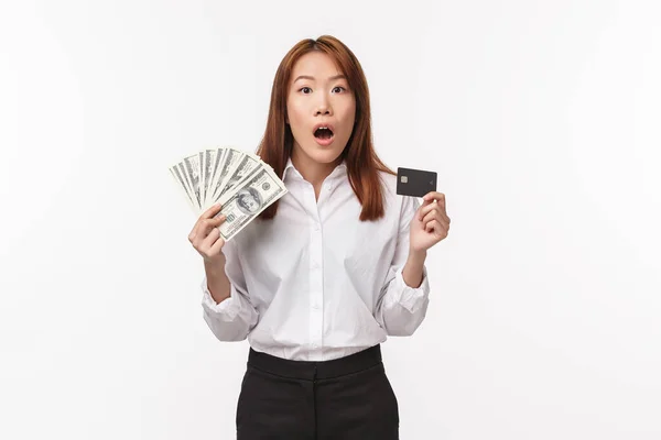Ekonomi, pengar och shopping koncept. Spännande och chockad ung asiatisk kvinna som innehar dollar och kreditkort, titta på kameran nervöst, vill slösa pengar på semester, fatta beslut, vit bakgrund — Stockfoto