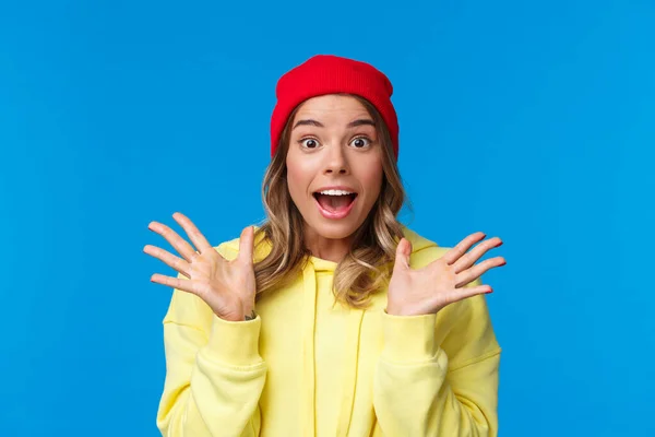 Emocionada mujer europea de buen aspecto explicar grandes noticias, hablando con un amigo sorprendido, estrechando la mano emocionado y mirando cámara fascinado, de pie fondo azul en gorro rojo —  Fotos de Stock