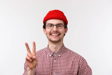 Yakışıklı, mutlu, beyaz bir adamın yakın plan portresi, barış jesti ve kamera dostu, resmi olmayan selamlama, hippi beresi ve gözlük takan, beyaz arka plan