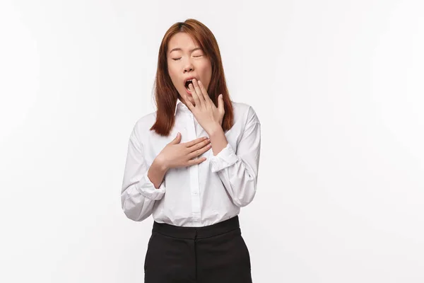 Portrait of bored or tired office lady, asian business woman in white shirt and black skirt, cover opened mouth as yawning from fatigue, working late on project, wake-up early morning — Stok Foto