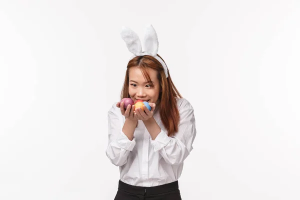 Vacanze di Pasqua, concetto di celebrazione. Ritratto di divertente donna asiatica nelle orecchie di coniglio, avida e stupita delle uova dipinte come se raccontasse il mio prezioso sfondo bianco in piedi — Foto Stock