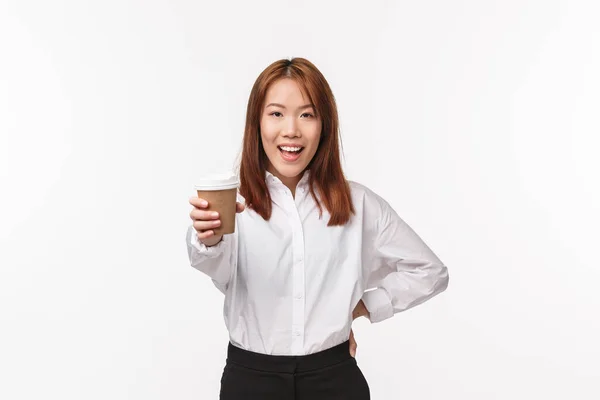 Office work, people and business concept. Energized cheerful asian woman suggest drink, give you cup of coffee and smiling say here you are, treating friend in cafe, standing white background — Stock Photo, Image