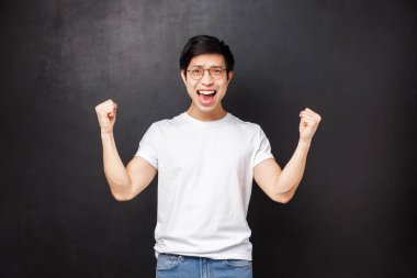 Mutlu ve tatmin olmuş Asyalı genç adam takımını galibiyetle kutluyor, amacına ulaşıyor, şampiyon gibi ellerini sıkıyor, başarıyı kutluyor evet diyerek zaferi kutluyor, zafere karşı zafer kazanıyor, siyah arka plan