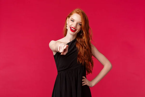 Conceito de moda, luxo e beleza. Retrato de mulher ruiva atrevida e assertiva em vestido preto e maquiagem à noite, apontando para a câmera convidando você para a festa, incentivar a dançar juntos — Fotografia de Stock