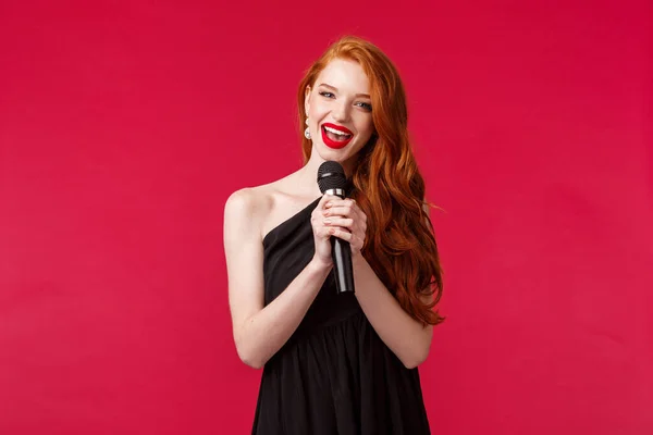 Siyah elbiseli, elinde mikrofonla karaoke yapan ya da halkın önünde kırmızı arka planda şarkı söyleyen muhteşem kadın portresi. — Stok fotoğraf