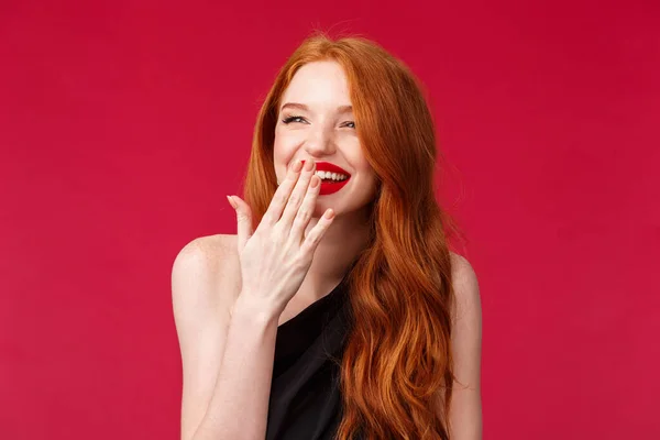 Close-up retrato de muito elegante jovem mulher europeia com cabelos longos encaracolados vermelho, vestido preto e maquiagem à noite, rindo sobre algo engraçado olhando para longe e cobrir o sorriso com palma — Fotografia de Stock