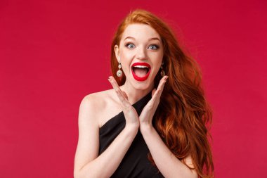 Makyaj, güzellik ve kadın konsepti. Heyecanlı, genç, kızıl saçlı, kırmızı rujlu, siyah elbiseli, alkışlayan, mutlu gülümseyen bir kadının yakın plan portresi.