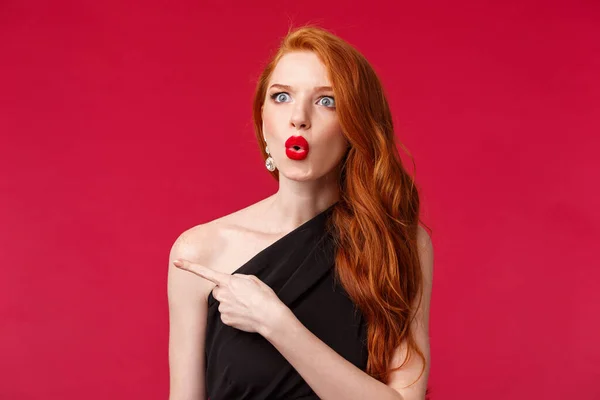 Close-up retrato de impressionado animado e sem palavras mulher ruiva atraente, vestindo vestido preto, batom vermelho e maquiagem à noite. olhar assustado dizer wow apontando esquerda questionado — Fotografia de Stock