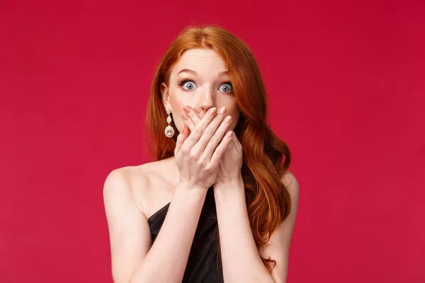 Close-up portrait of speechless, shocked and concerned young redhead woman found out someones terrible secret, gossiping, gasp and cover mouth with hands, standing red background — Stock Photo, Image