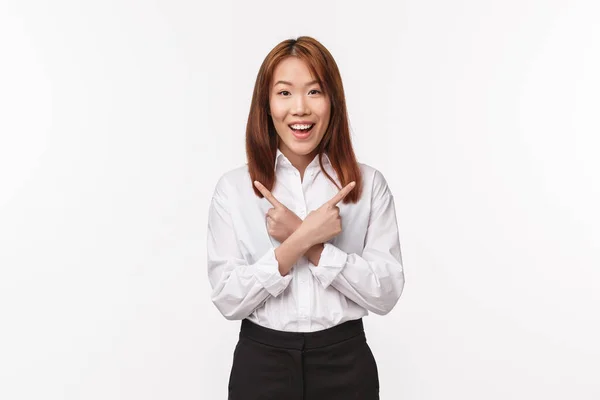 웃고 있는 아시아 여성, 흰 셔츠를 입고 사무실 직원, 두 가지 선택에서 좌우 손가락을 가리키고 있는 행복 한 사진, 조언을 구하고 있는 변형 이 거의 없는, 밝고 흰 배경의 카메라처럼 보이는 — 스톡 사진