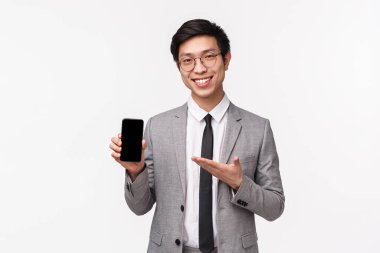 Zeki ve yetenekli Asyalı iş adamının belden yukarı portresi toplantıda akıllı telefonlar için yeni bir uygulama tanıt, cep telefonu tut, alet göstergesine işaret et, gülümse, tavsiye indir