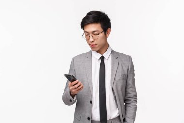 Gri takım elbiseli, ciddi görünümlü, stil sahibi bir iş adamının belden yukarı portresi, el ele tutuşmak, cep telefonu kullanmak, iş ortağıyla mesajlaşmak, akıllı telefon kullanmak, beyaz arka plan