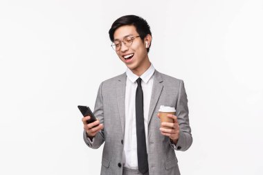 Ofis çalışanları, iş ve yaşam tarzı konsepti. Şanslı Asyalı girişimcinin belden yukarı portresi kablosuz kulaklık kullanarak arkadaşını arıyor, akıllı telefonu tutuyor ve kahveyi alıp götürüyor, gülümsüyor.