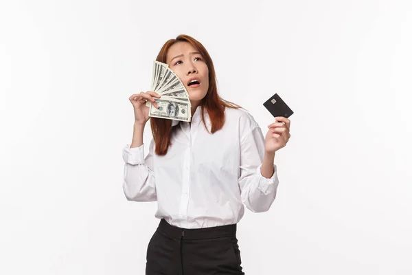 Success, women and career concept. Satisfied pleased and boastful young asian female enjoying being rich, holding credit card and brush cheeks with dollars, have lots money, white background