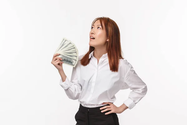 Portrait of good-looking successful asian woman in white shirt, businesswoman tired of being rich, waving money trying to cool herself look up relieved, become rich, white background — Stock Photo, Image
