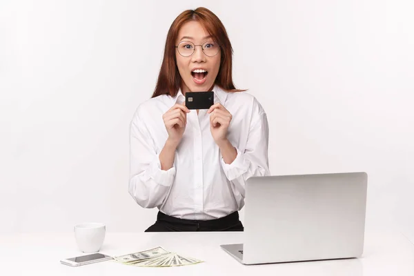 Concepto de carrera, trabajo y mujeres empresarias. Primer plano retrato alegre joven asiática sentada en la oficina con el ordenador portátil, dinero, celebrar la tarjeta de crédito, mirar divertido, consiguió el primer cheque de pago — Foto de Stock