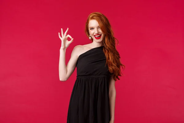 Элегантность, мода и женская концепция. Портрет сексуальной рыжей напористой молодой женщины в стильном элегантном черном платье, стройная модель в выпускном платье, показать хорошо, отличный жест улыбка приятно — стоковое фото
