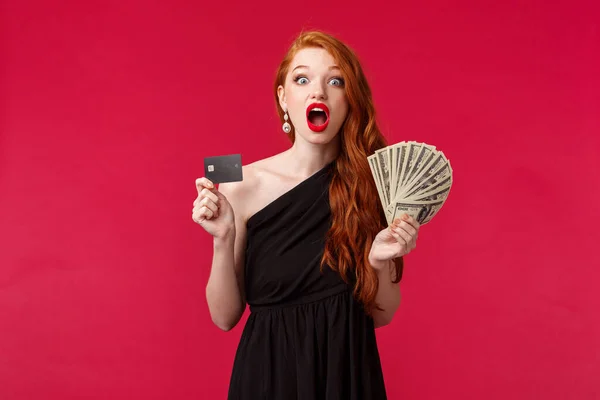 Concepto de lujo, belleza y dinero. Retrato de chica afortunada y sorprendida expresan incredulidad como premio receptor, miles de dólares, tienen fan de efectivo y tarjeta de crédito, se ven sorprendidos, fondo rojo — Foto de Stock