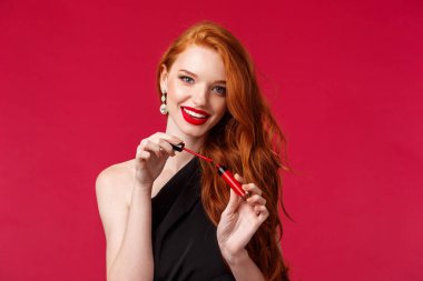 Makyaj, güzellik ve kadın konsepti. Siyah gece elbisesi giymiş, muhteşem, kadınsı ve şehvetli kızıl saçlı kadının yakın plan portresi. Restoran randevusuna hazırlanıyor, kırmızı ruj sürüyor ya da rimel sürüyor.