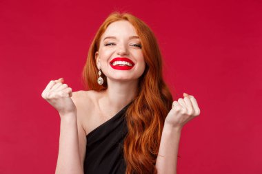 Kutlama, duygular ve güzellik konsepti. Şanslı genç, güzel, kızıl saçlı bir kadının yakın plan portresi. Siyah elbiseli, kırmızı dudak parlatıcısı, şampiyon dansı, zafer ve mutlu bir gülümseme.