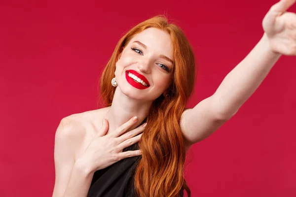 Portrait en gros plan d'une magnifique femme rousse souriante et heureuse profitant de sa fête d'anniversaire, prenant selfie pour les médias sociaux en robe noire élégante et look bal avec rouge à lèvres rouge, fond rouge — Photo