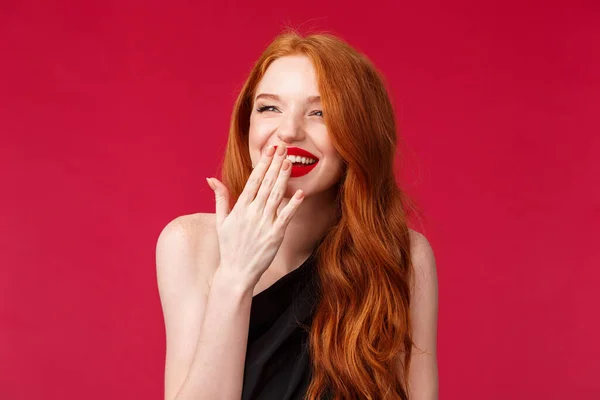 Close-up retrato de muito elegante jovem mulher europeia com cabelos longos encaracolados vermelho, vestido preto e maquiagem à noite, rindo sobre algo engraçado olhando para longe e cobrir o sorriso com palma — Fotografia de Stock