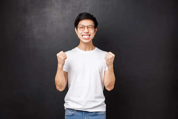 Yes I did it. Satisfied and happy asian guy passed exam, fist pump in success and celebration, wink joyfully smiling achieve goal, winning prize or reward, triumphing over victory, black background