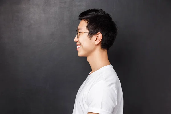 Profile portrait of happy smiling asian man in white t-shirt looking at left blank space, grinning friendly away as posing against black background, concept of people, emotions and advertising — Stock Photo, Image