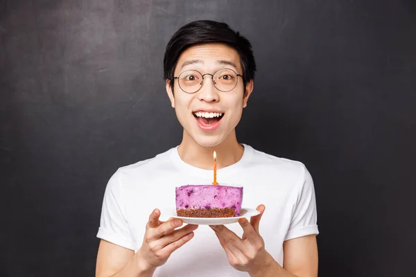 Celebration, holiday and birthday concept. Close-up portrait of amazed and happy young asian man holding b-day cake and smiling amused, throw party, blow out candle for making wish