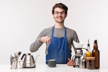 Barmen, kafe çalışanı ve barmen konsepti. Genç beyaz adam restoranda çalışıyor, içkileri karıştırıyor, çaydanlığın yanında duruyor, filtre kahve hazırlıyor, beyaz arka planda duruyor.