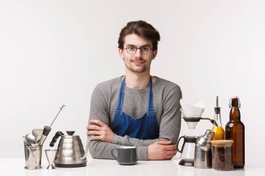 Barmen, kafe çalışanı ve barmen konsepti. Size nasıl yardımcı olabilirim? Önlük içinde çalışan sevimli genç bir erkek işçi, müşteriye kahve yapar, çaydanlığın yanında durur ve içer.