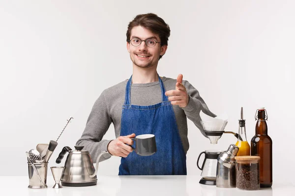 Barista, trabajador de cafetería y camarero concepto. Amistoso chico caucásico agradable en delantal hacer gesto pistola dedo y sonriendo al cliente mientras se prepara la bebida, hacer café, de pie fondo blanco — Foto de Stock