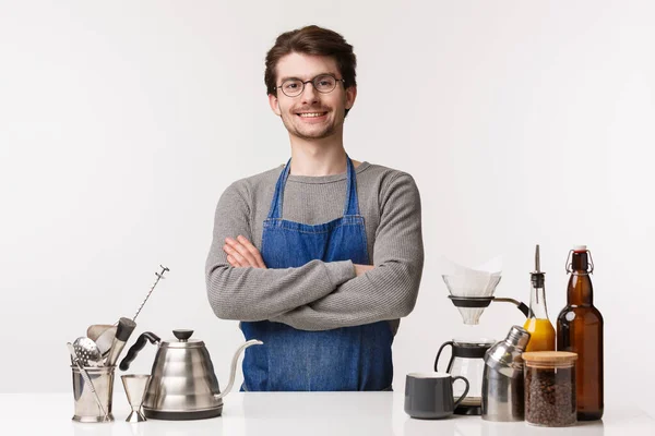 Barista, trabajador de cafetería y camarero concepto. Joven profesional de aspecto serio en delantal preparar café, trabajar en el restaurante, de pie cerca del escritorio con tetera, y tazas, fondo blanco — Foto de Stock