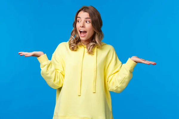Girl weighing two choices as making decision, look away picking between products she holding in arms on left and right side, standing excited over blue background — Stock Photo, Image