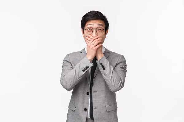 Midja upp porträtt av mållös och förvånad asiatisk ung kontorschef i kostym, affärsman skvallrar om något chockerande, täcka munnen och uttrycka vördnad med ögon, vit bakgrund — Stockfoto
