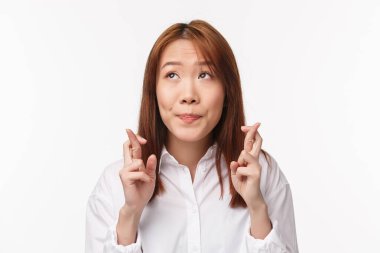 Yakın plan portre Asyalı umut dolu ve ürkek bir kadın hayalperest ve düşünceli, aptal bir gülümsemeye bakıyor, şans diliyor, dilek rüyası gerçek oluyor, beyaz arka plan duruyor.