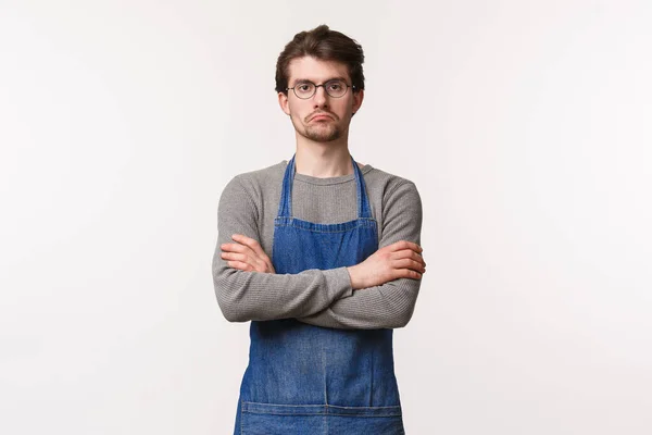 Serious-looking skeptical male manager looking at employees watching how they work, grumpy staring camera cross hands over chest, being disappointed or reluctant, stand in apron at coffee shop