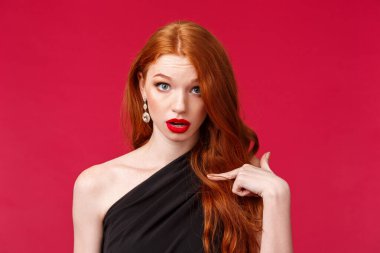 Kim, ben mi? Şok olmuş ve şaşırmış siyah elbiseli kızıl saçlı kız sorgulanmış ve kafası karışmış görünüyor. İnançsız bakışlar kendini işaret ediyor gibi, seçilmiş ya da suçlanmış, kırmızı arka planda.