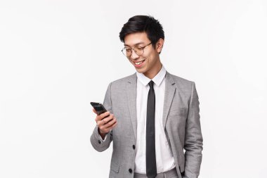 Teknoloji ve finans kavramı. Memnun olmuş yakışıklı girişimcinin belden yukarı portresi, gri takım elbiseli şirket sahibi, akıllı telefondan iyi bir mesaj alırken gülümseyen, beyaz arka plan