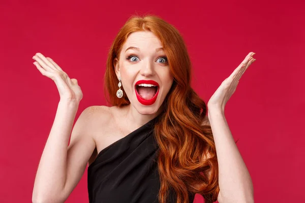 Celebration, emotions and beauty concept. Close-up portrait of happy cheerful redhead woman winning, triumphing over excellent great news, raise hands up and scream joyful, red background