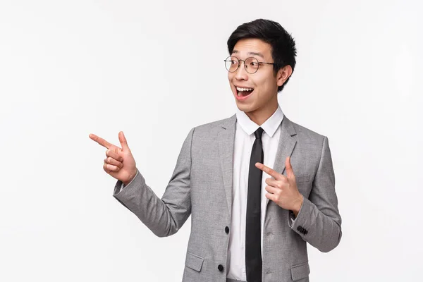 Porträtt av entusiastisk snygg, framgångsrik asiatisk affärsman nöjd med diagram, positiva resultat, ökad inkomst, pekfingrar vänster och ser glada leende, bära kostym — Stockfoto